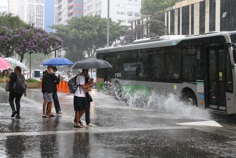 Ônibus joga água na calçada durante chuva na Avenida Paulista.