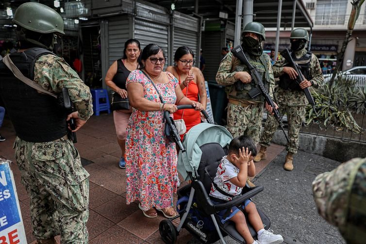 People walk past armed soldiers, as they guard a commercial area, in the aftermath of a wave a violence that saw the storming of a TV station on-air and explosions around the nation, in Quito, Ecuador, January 11, 2024. REUTERS/Ivan Alvarado
